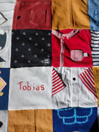 Détail de la couverture souvenir garçon personnalisée avec son prénom brodé. La couverture personnalisée unique est confectionnée en France à partir des habits troué ou salit. Redonnez vie à ses tenues.